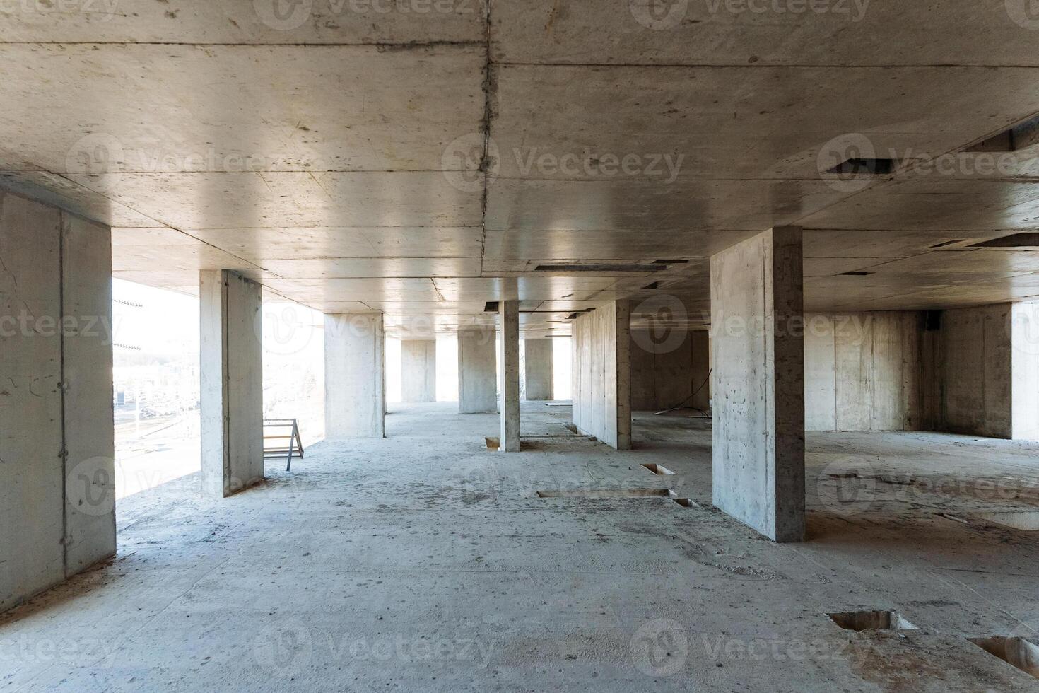 A large, spacious empty room featuring unfinished concrete walls and sturdy pillars, all situated within a building that is currently under construction and is not yet complete photo