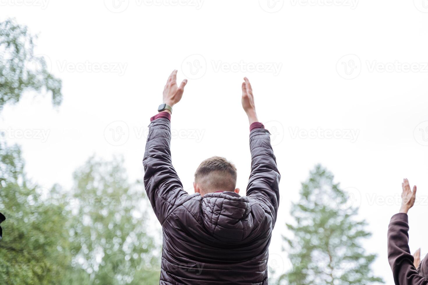 In a picturesque natural environment, a cheerful group of individuals energetically lift their hands with joy under the clear sky, showcasing genuine happiness and excitement photo