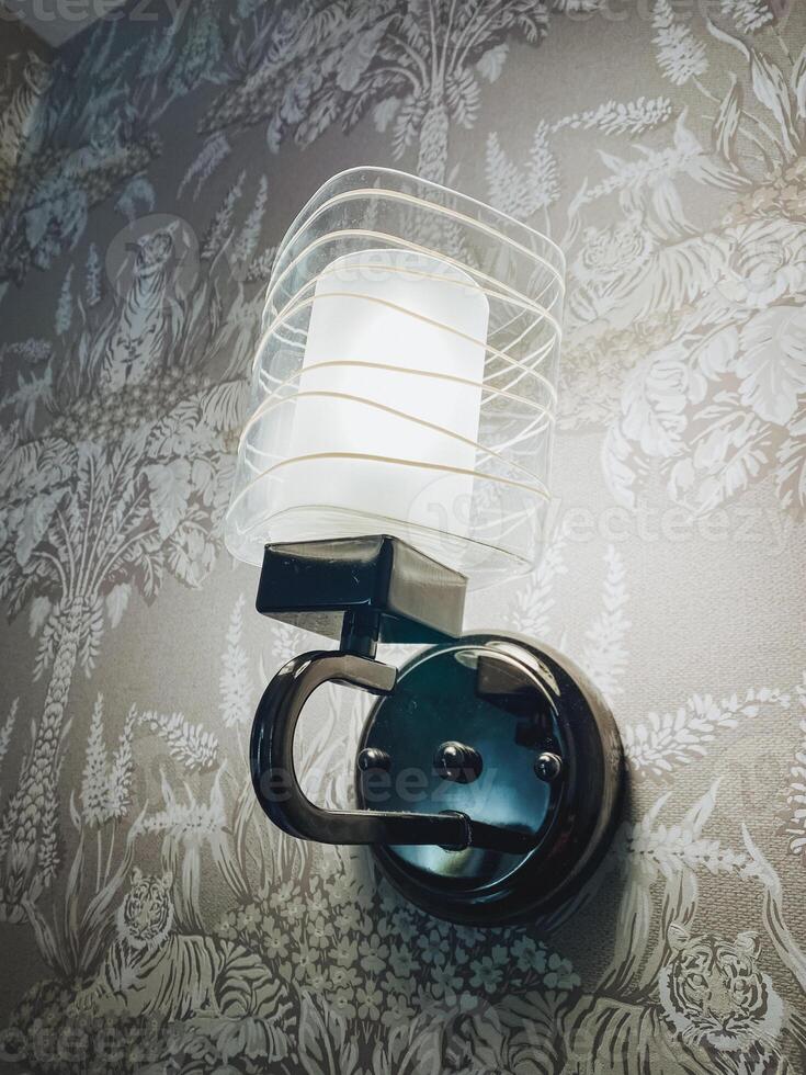 A stylish wall light is elegantly hanging on a beautifully patterned piece of wallpaper, creating a lovely ambiance in the room that enhances its decor and overall aesthetic appeal photo