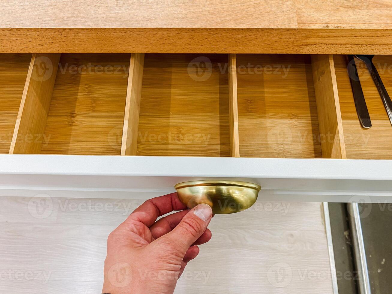 A person is in the process of carefully opening a wooden drawer that features a classic brass handle, revealing the interior of the furniture piece and its potential contents photo