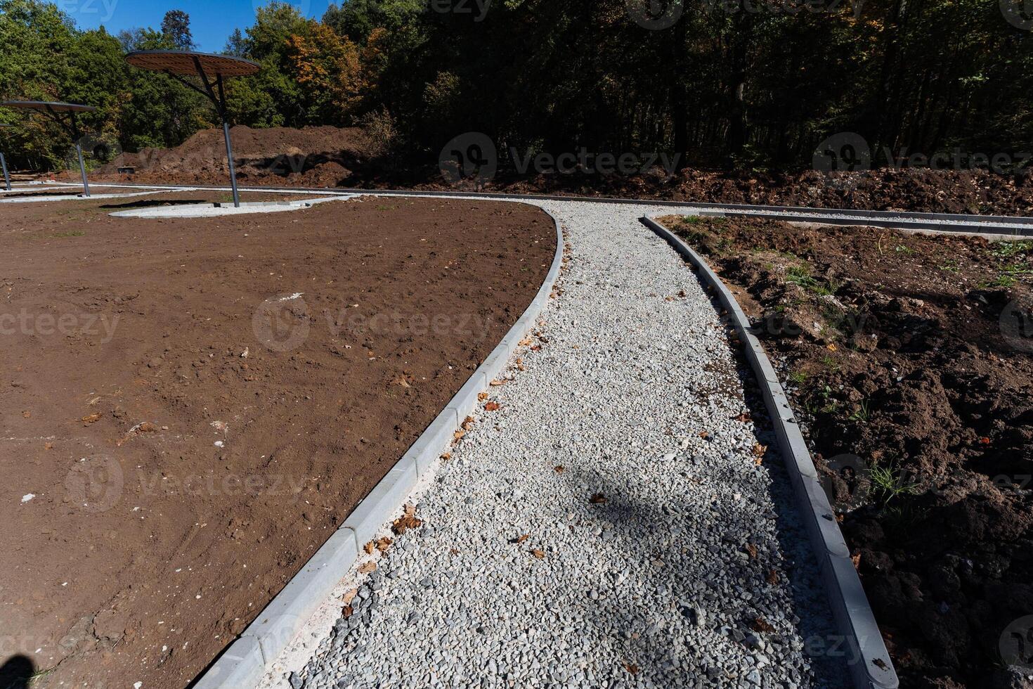 A lovely and charming gravel path winds its way through a vast and expansive dirt field, with magnificent towering trees in the background, creating a truly picturesque natural scene photo