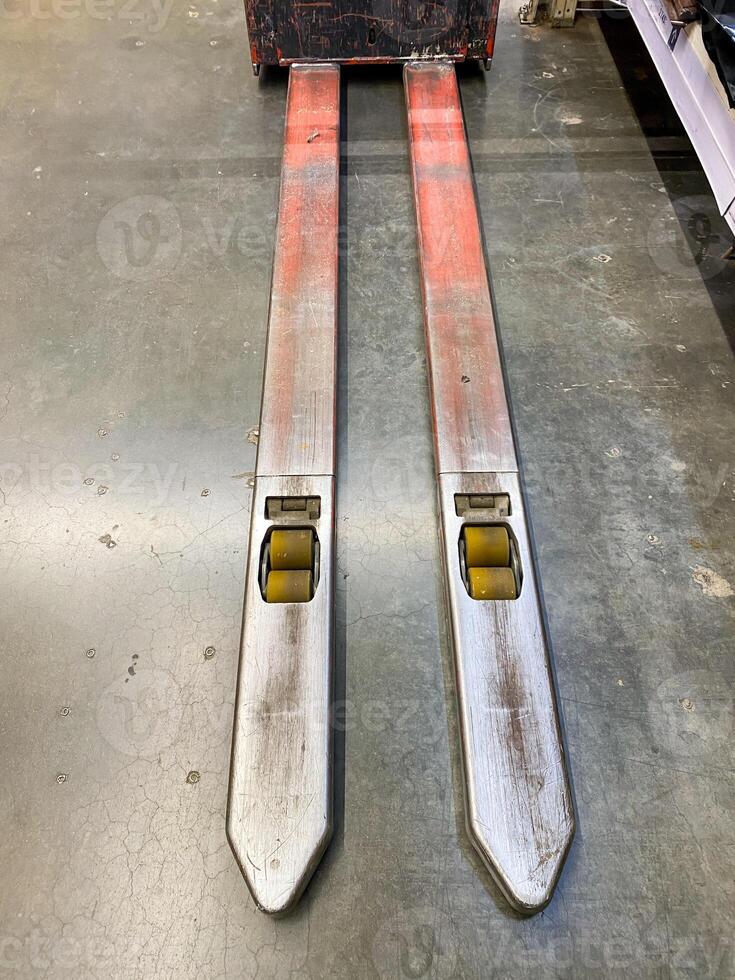 A pair of forklift forks is resting on a solid concrete floor, awaiting use in various lifting operations that they are designed for, showcasing their robust construction and utility photo
