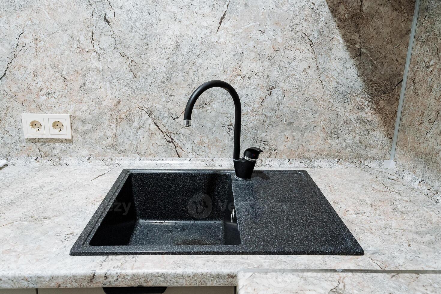 In a beautifully designed kitchen, there is a sleek, black sink accompanied by a stylish black faucet, both elegantly set on a counter that enhances the overall aesthetic of the space photo