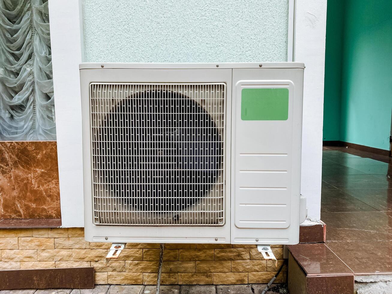 A white air conditioning unit is securely mounted on the exterior of a tall building, providing essential cooling and effective ventilation for the comfort of the occupants inside the rooms photo