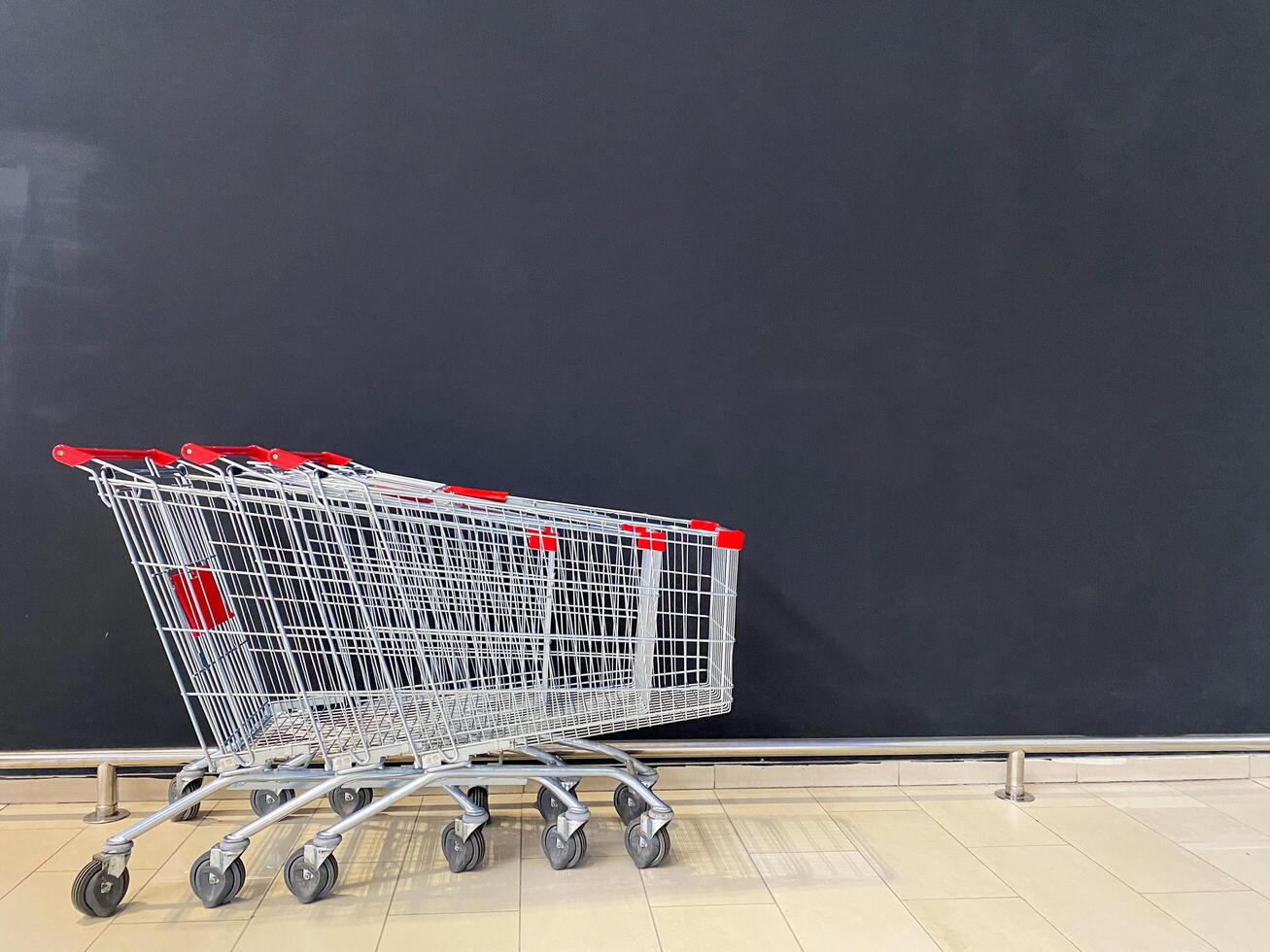 In a row, there are three shopping carts neatly lined up, positioned right in front of a large blackboard, creating an interesting visual and functional comparison between them photo