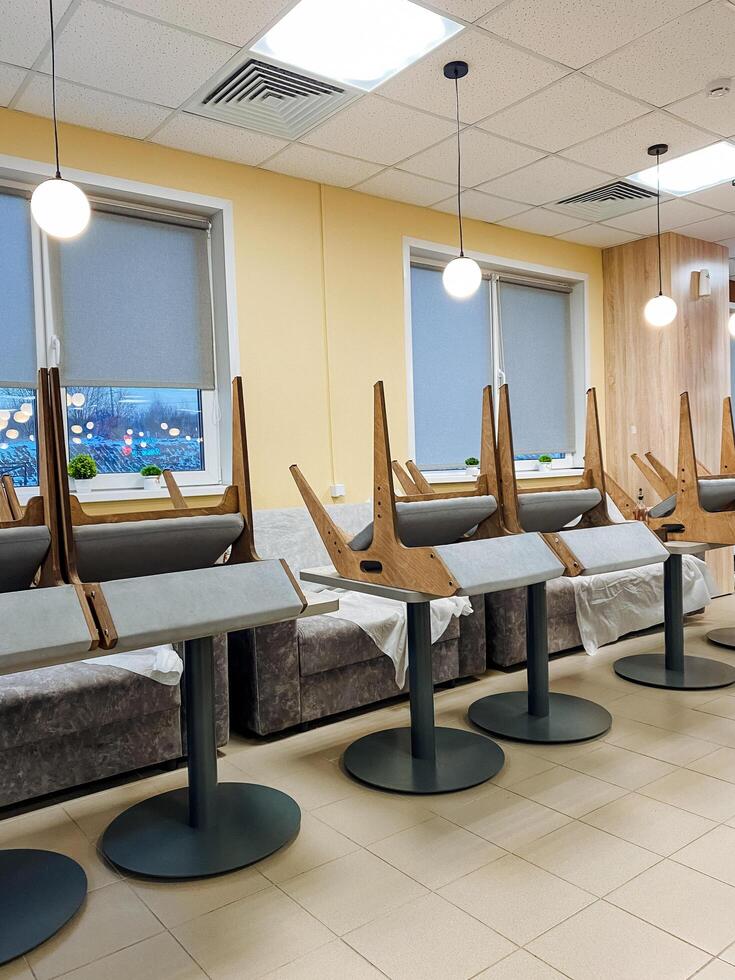 In a spacious room, there exists a long row of tables, accompanied by chairs that are neatly arranged, which collectively contribute to the overall design and ambiance of the interior space photo