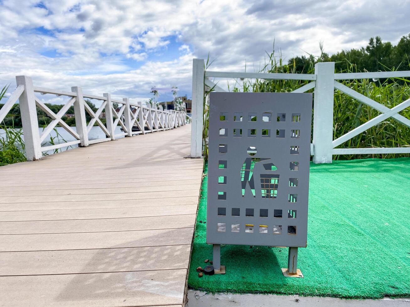 On a vivid green mat, there is a trash can placed conveniently right next to a sturdy wooden bridge, creating a charming outdoor scene filled with natural beauty and tranquility photo
