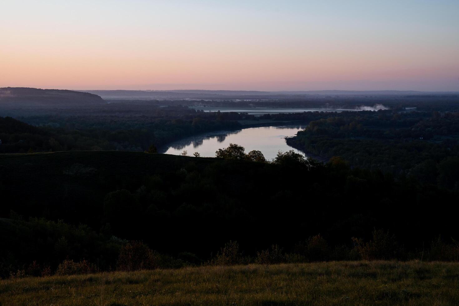 A serene lake is embraced by trees on a hill under the sunset sky photo