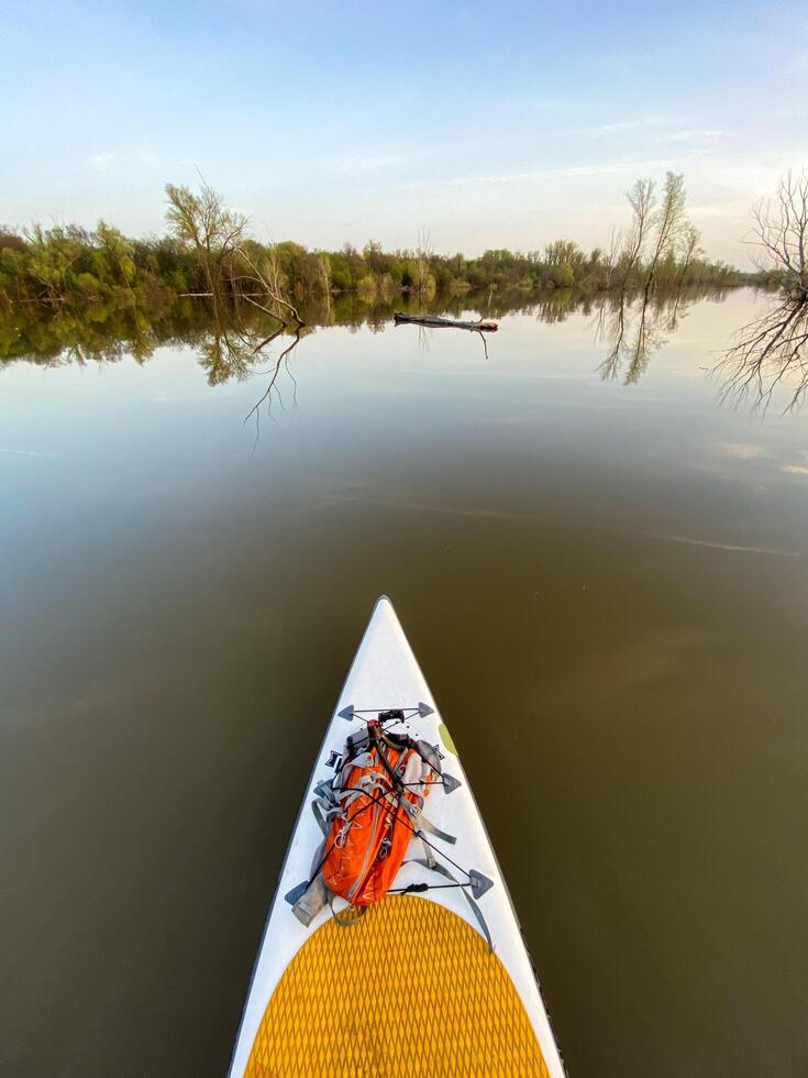Experience the tranquility of paddleboarding on a serene river at dusk, embraced by lush greenery and calm waters photo