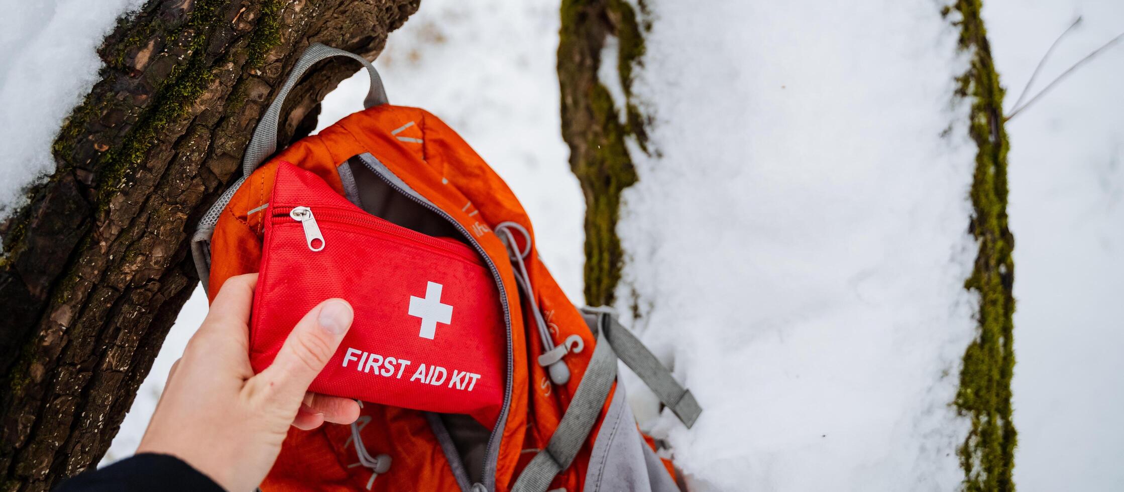 A person is standing and holding a first aid kit right in front of a wellused backpack which is likely packed with essentials for their outdoor activities or adventures ahead photo