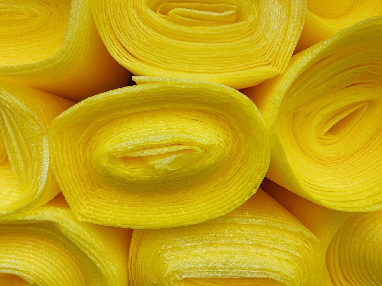 A collection of bright yellow rolls of fabric are carefully stacked on top of one another, creating a visually interesting display and showcasing their vibrant color and texture photo