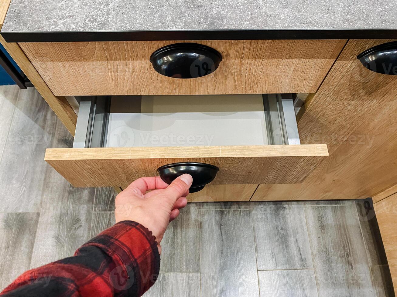 A person is thoughtfully opening a beautifully crafted wooden kitchen drawer, examining its various contents and appreciating the exquisite craftsmanship of the wood and design photo