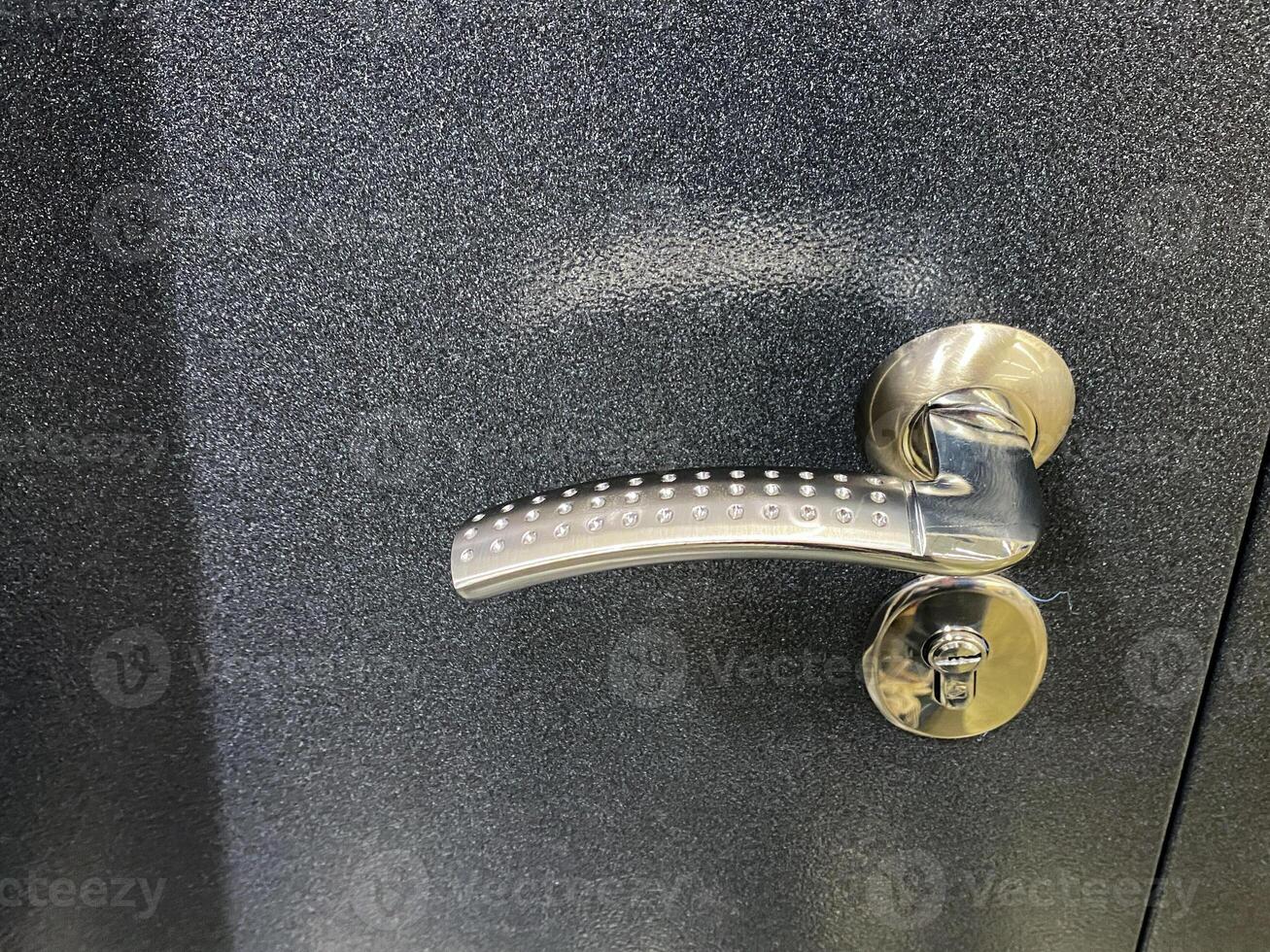 The image showcases a closeup of a modern black door handle, emphasizing its unique design, texture, and intricate hardware details, creating a visually striking appearance photo