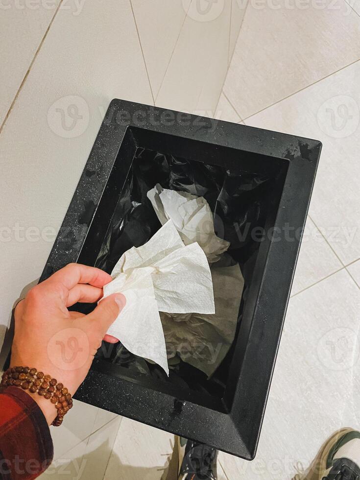 An individual is carefully placing used tissues into a trash can, demonstrating a simple yet meaningful gesture of disposing of waste responsibly. Their focus is evident in the action photo