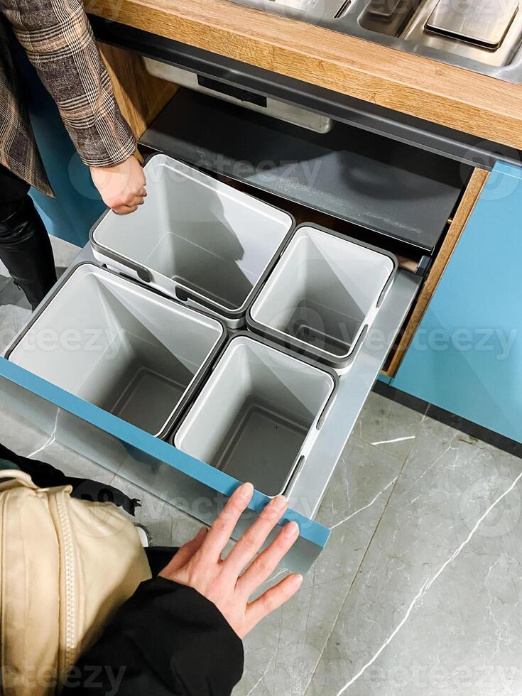 A person is diligently and carefully reaching into a wellorganized drawer that contains three distinct bins, likely searching for an urgently needed item that they require at this moment photo