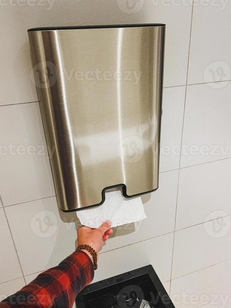 A person is currently utilizing a paper towel dispenser located in a bathroom, efficiently drying their hands after washing them, making use of this practical hygiene feature photo