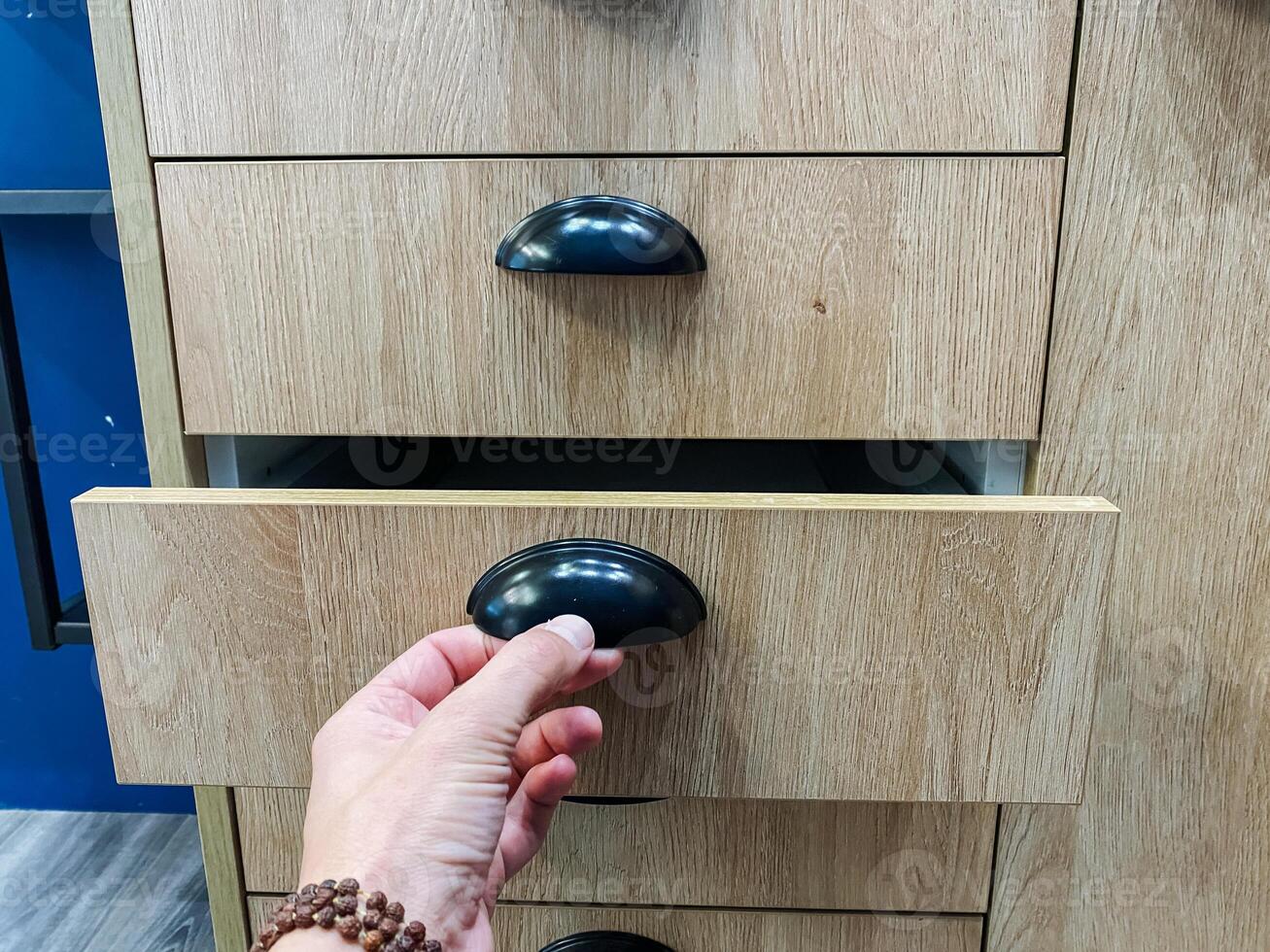 A person is opening a wooden drawer that features a sleek black handle, showcasing its craftsmanship and design, creating a sense of functionality and elegance in a home environment photo