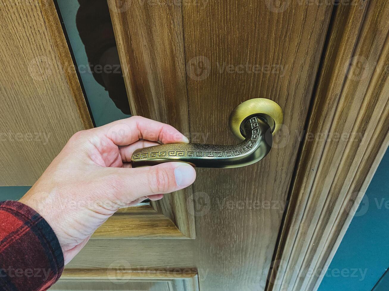 A hand clasping a vintage brass door handle positioned on an elegantly designed wooden door creates a charming and inviting entrance photo
