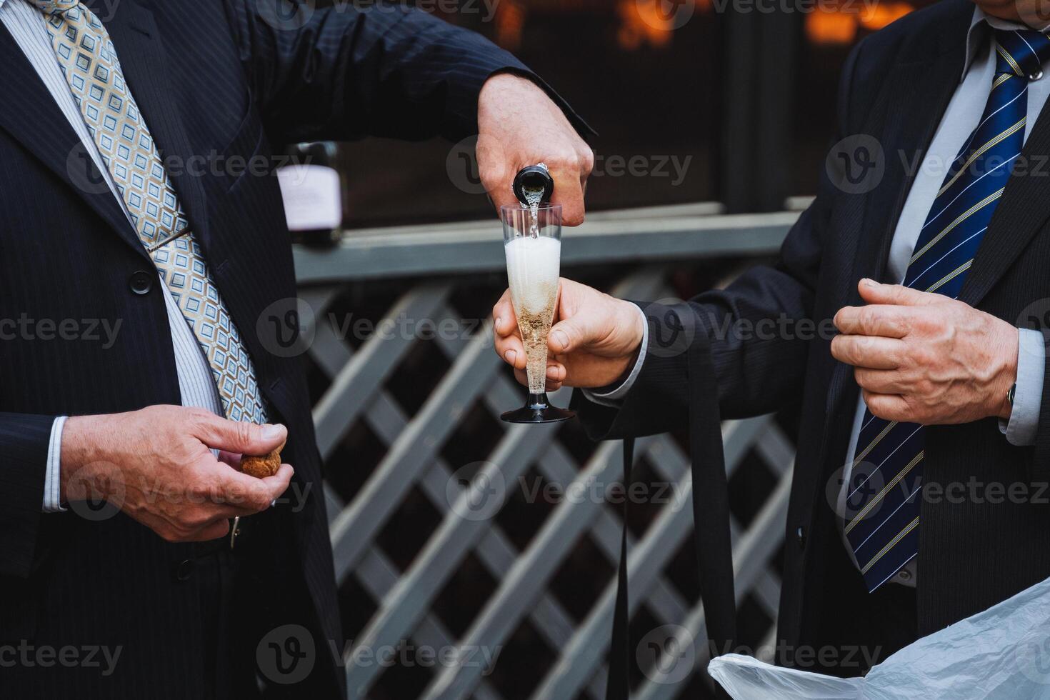 Two men in formal wear are clinking champagne glasses in a celebratory gesture photo
