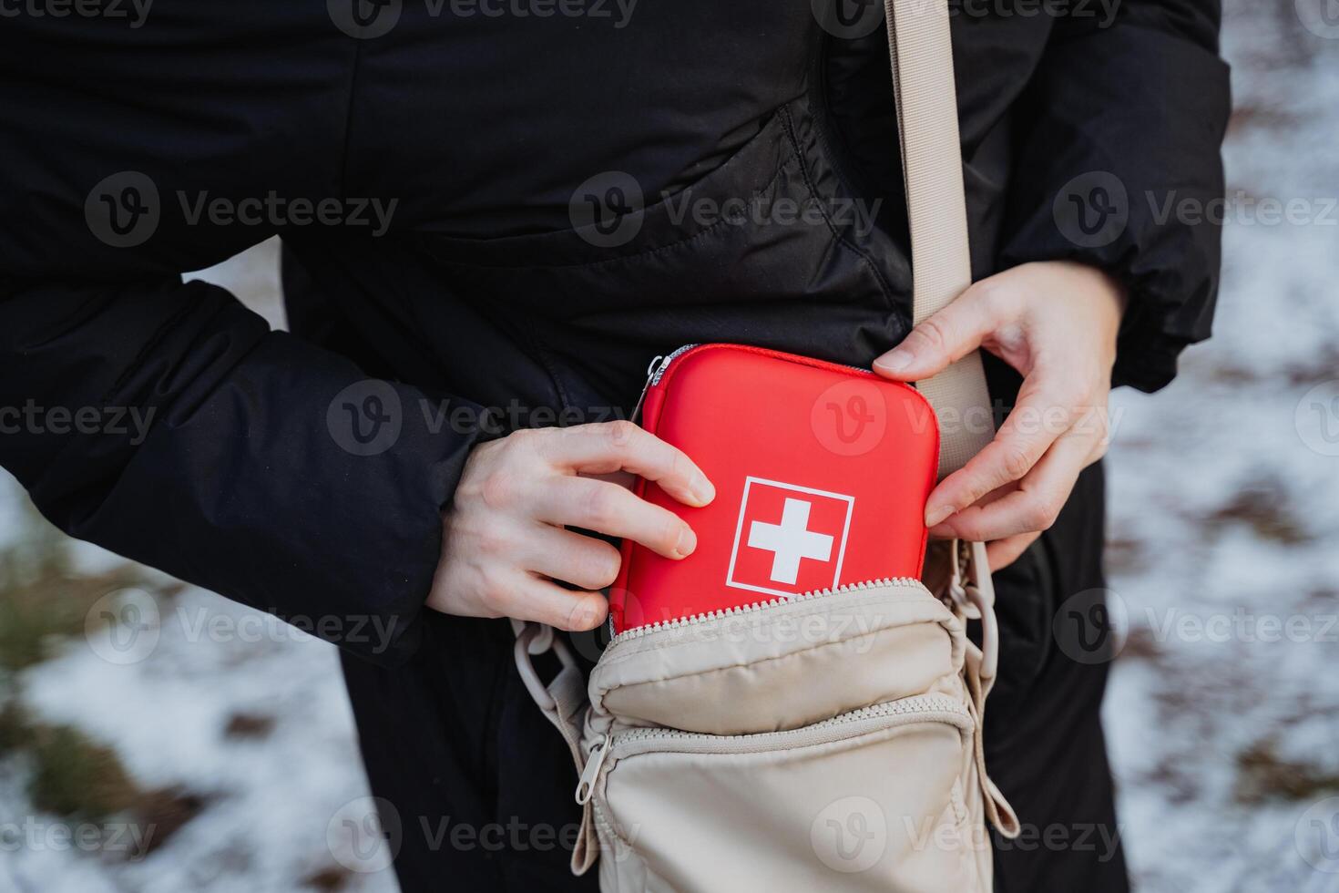 An individual is carefully placing a first aid kit inside their purse. This action demonstrates preparedness for any potential emergencies that may arise during their day photo