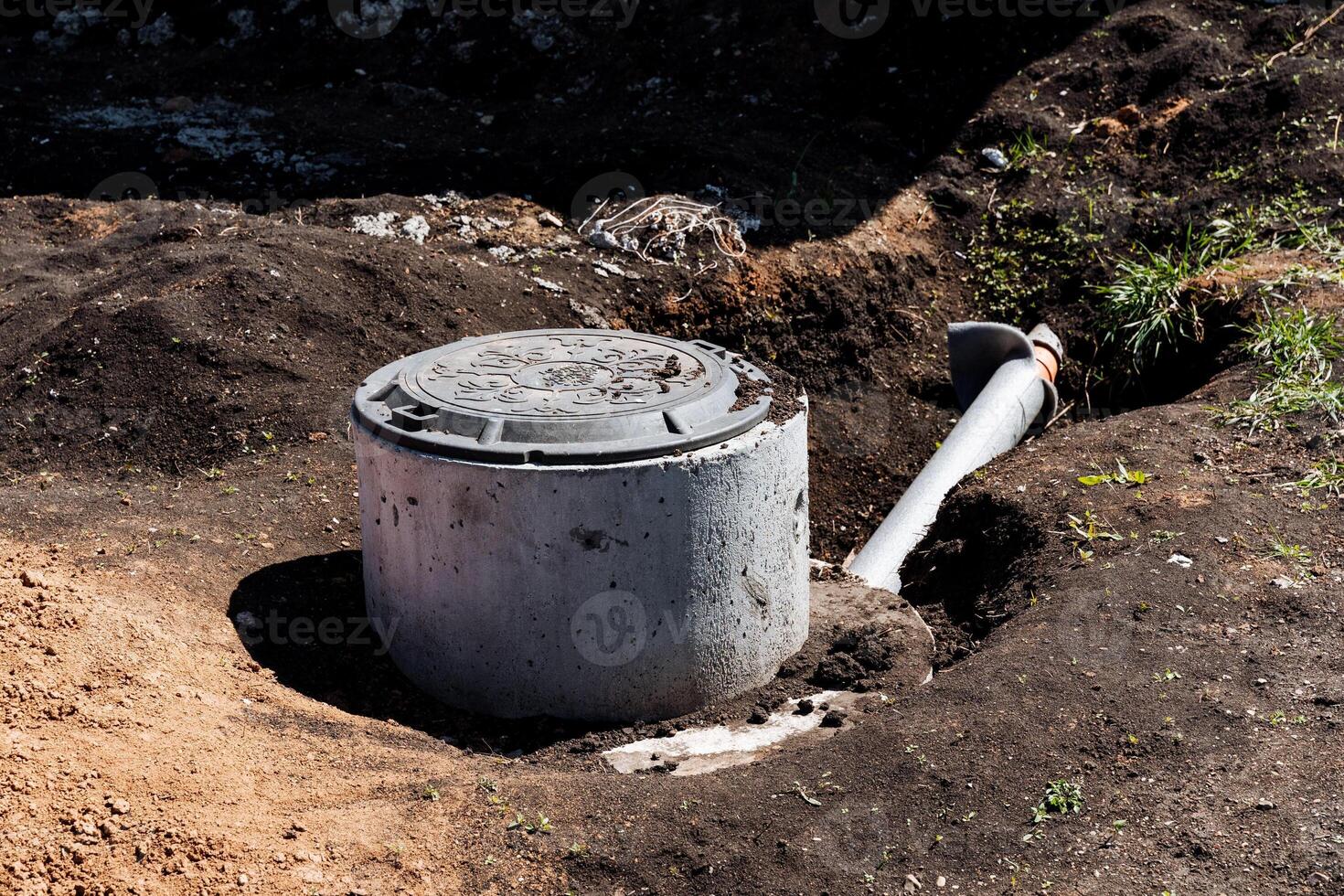 Concrete septic tank sits in dirt by pipe, surrounded by grass and rocks photo