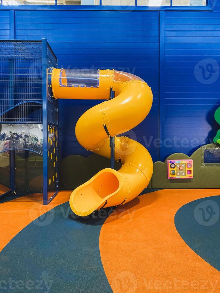 In a vibrant playground setting, there is a bright yellow spiral slide that stands out, complemented by an eyecatching blue wall positioned just behind it, creating a lively atmosphere photo