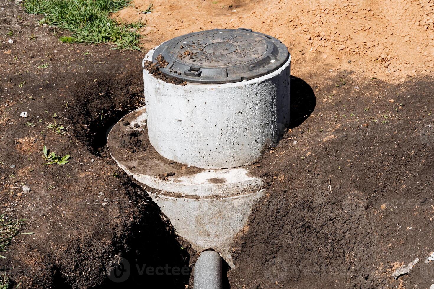 Concrete ring on dirt by pipe in yard, surrounded by soil and grass photo