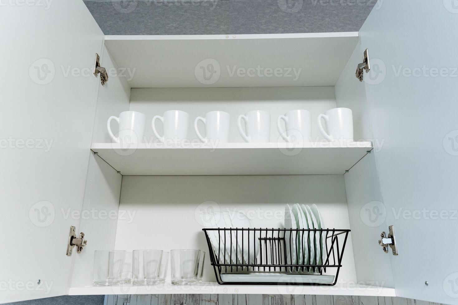 A wellstocked kitchen cabinet that is filled with a wide variety of cups and glasses, along with a practical dish drying rack that allows for easy access and optimal organization photo