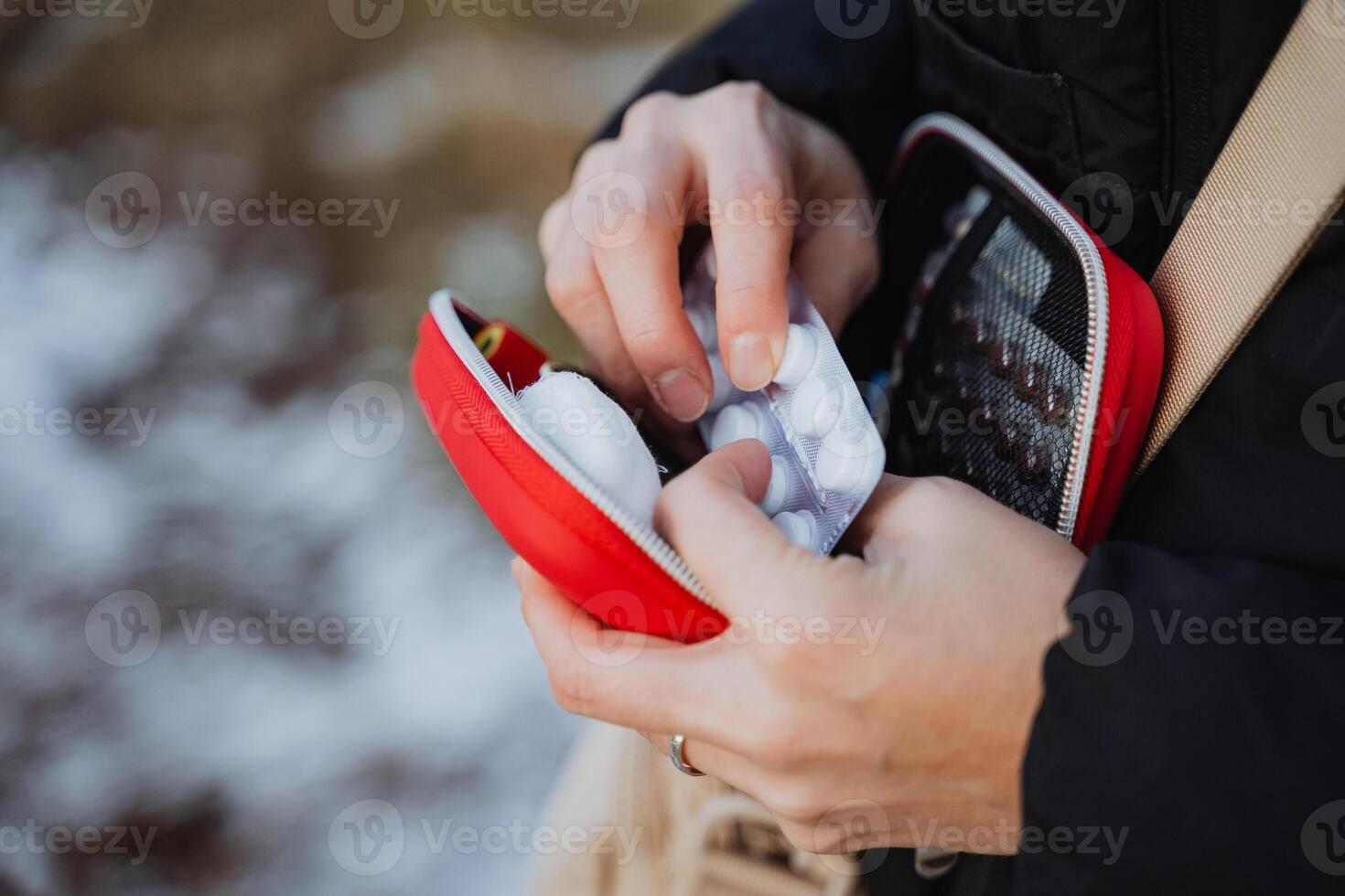 A person is carefully taking a small pill out of a bright red case that is designed for holding medication and vitamins while ensuring to use their fingers and thumb appropriately photo