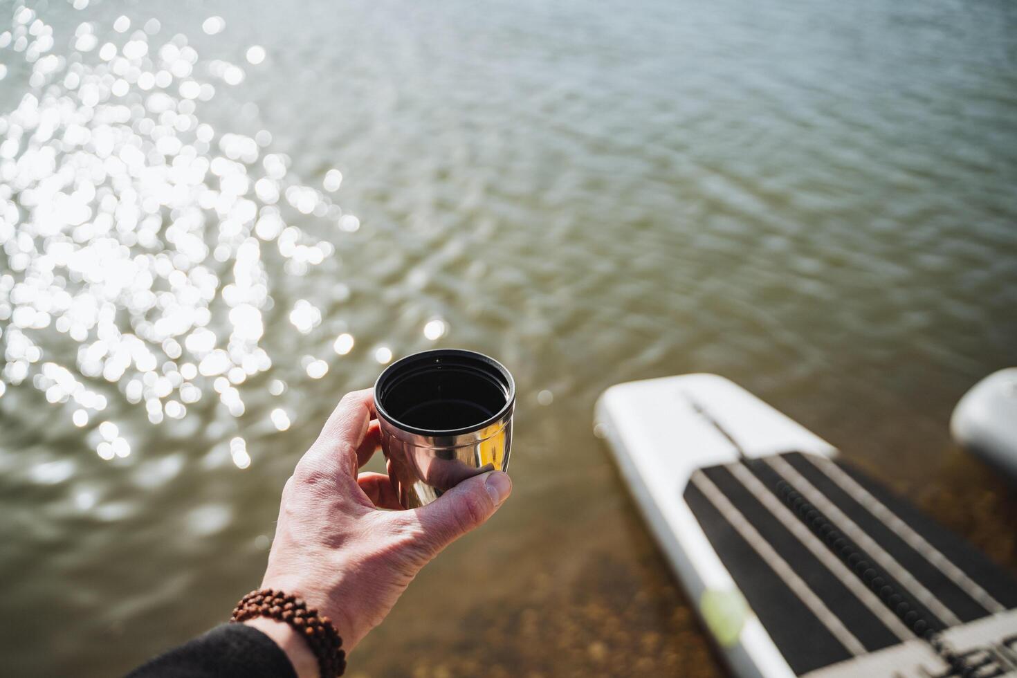 A mug from Terpmos in the hand of a person on the background of water, hiking on the water, a glass of tea in nature, a hand holding a mug with coffee. photo