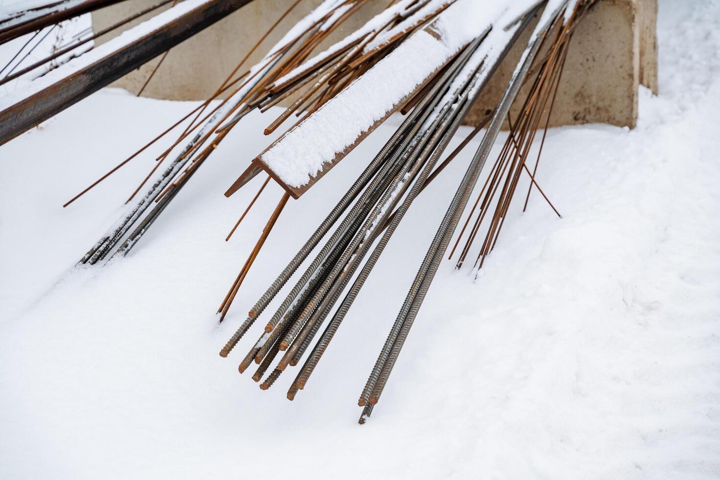 Beneath a thick, white layer of freshly fallen snow lies a heavy, hidden pile of rusty, aged metal bars, starkly contrasting with the frigid winter landscape surrounding them photo