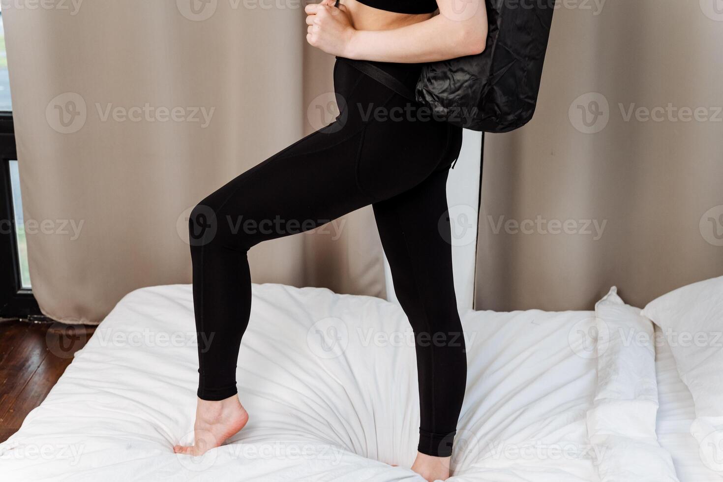 A woman in sportswear standing on a bed showcases her trendy style. Her look is sporty yet elegant with a touch of casual chic, highlighting her leg and knee for a fashionable appeal photo