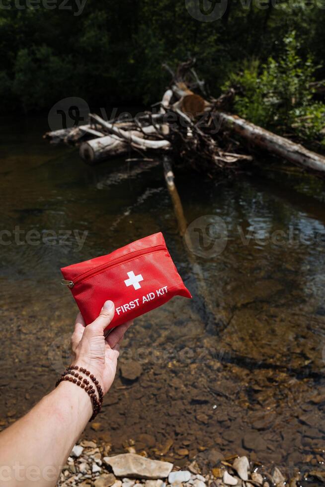 Illustrating the significance of readiness in the wilderness, an individual with a first aid kit is seen beside a river in a natural setting. Essential for outdoor excursions photo