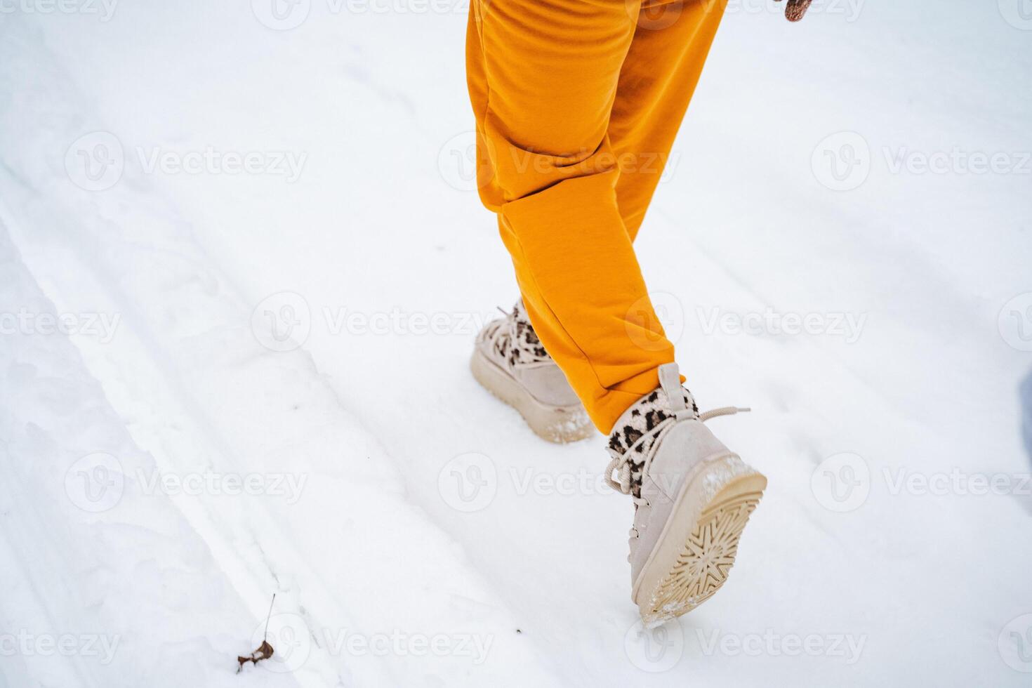 A person who is wearing bright yellow pants and stylish white boots is walking through the thick snow, enjoying the chilly winter day and the beauty of the icy landscape all around them photo