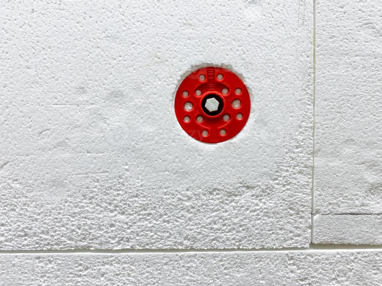 A Red Fire Sprinkler Head is securely mounted on a clean, white wall, serving as an essential safety feature in the buildings fire protection system photo