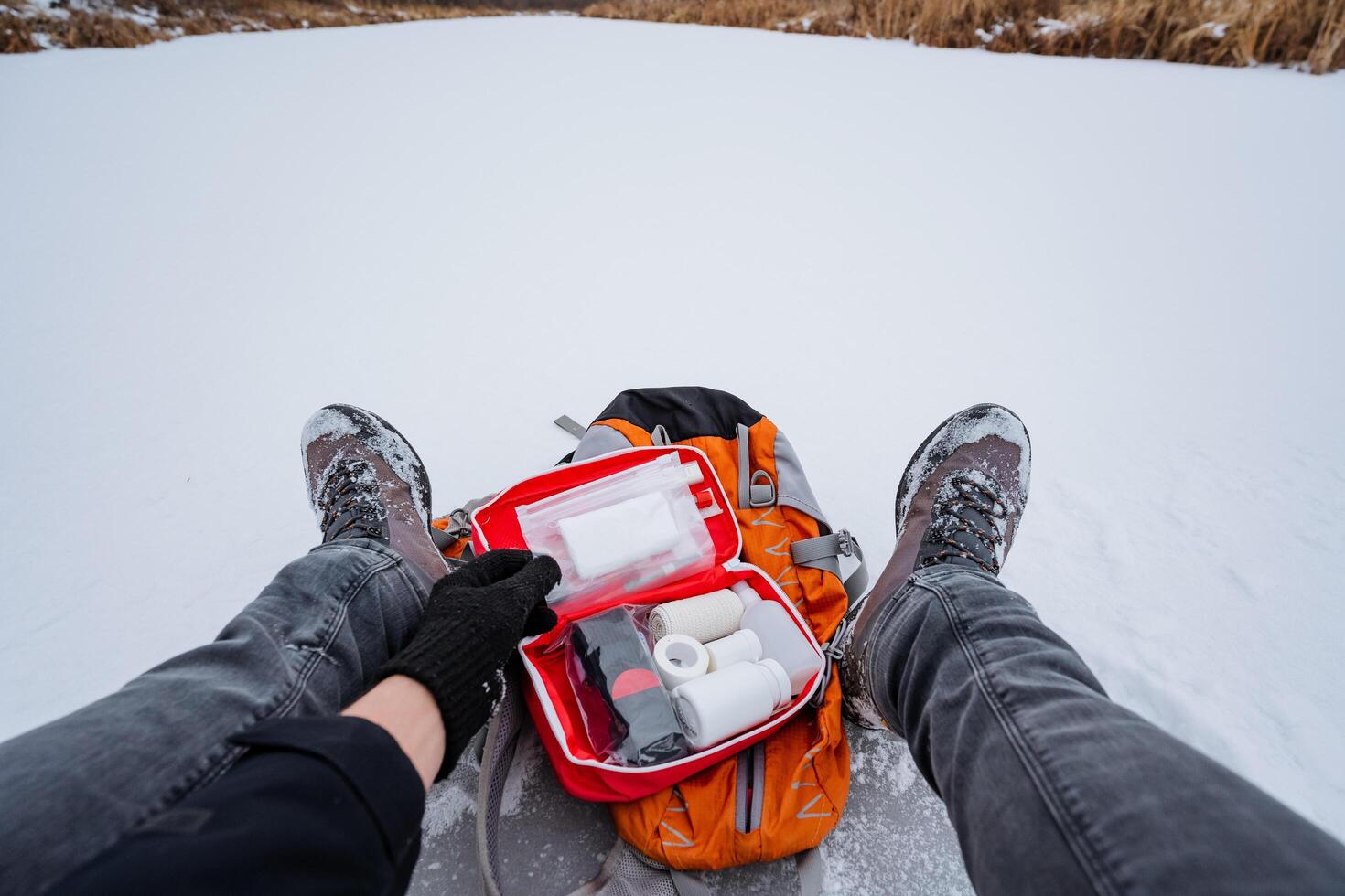 A person is laying in the snow, bundled up and holding a first aid kit firmly in their hand, ready to assist in an emergency while surrounded by a beautiful winter landscape photo