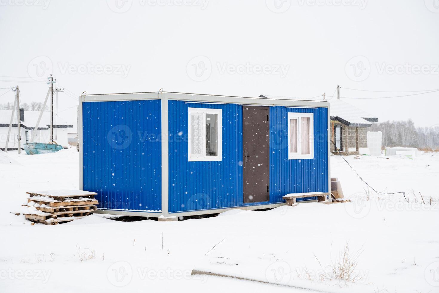 A vibrant blue container house is prominently situated right in the middle of a vast snowy field, surrounded by the beautiful winter landscape and crystalclear ice formations photo