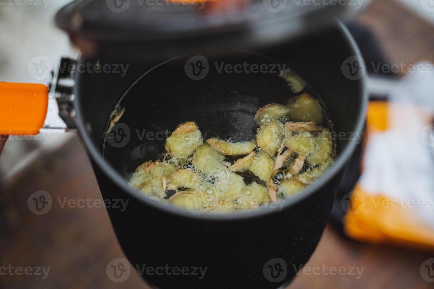 Pieces of ginger are boiled in boiling water in a saucepan, the lid of the cauldron is ajar, making a hot drink, ginger warming tea. photo