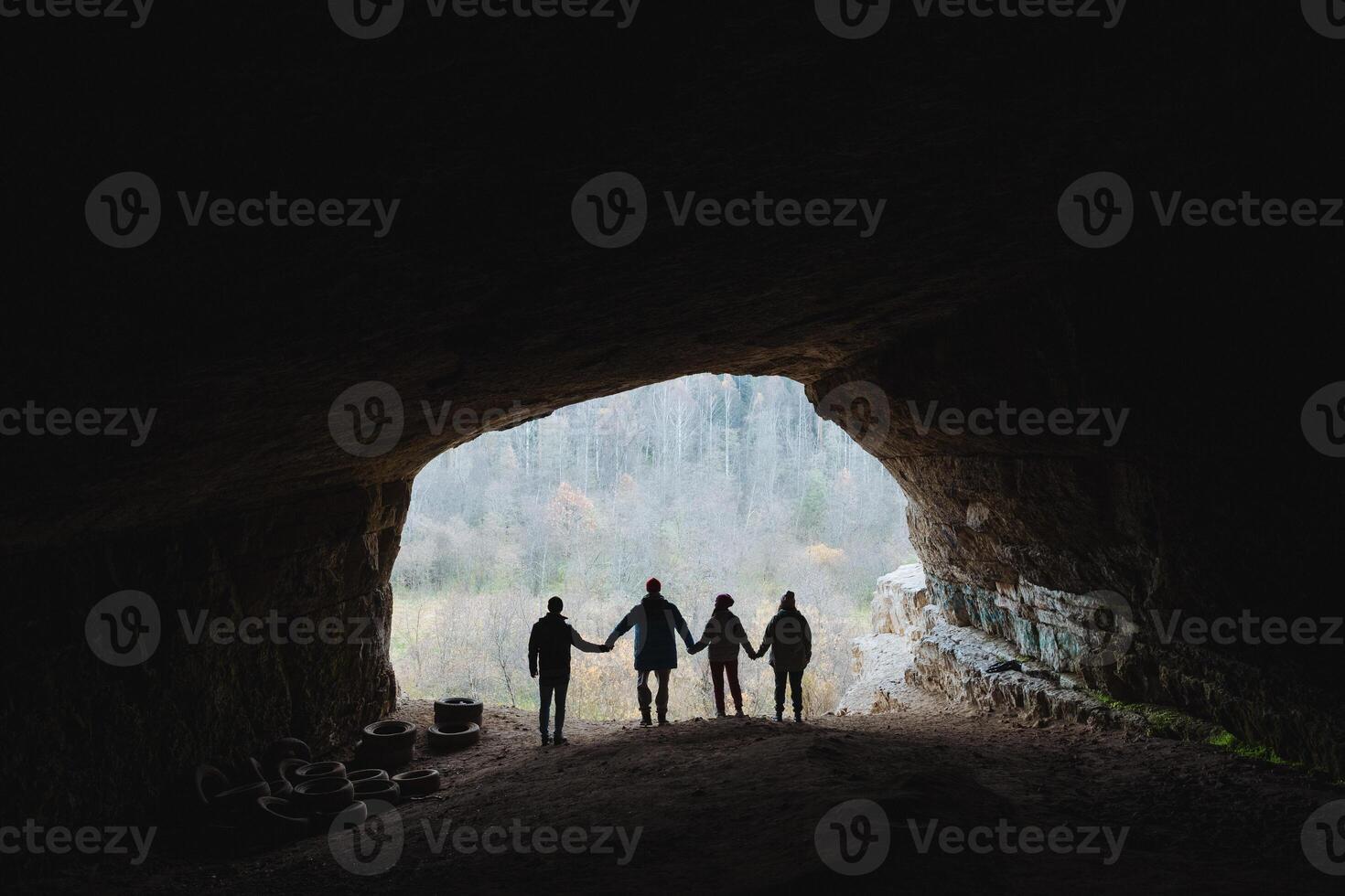 A diverse group of individuals is present in a dimly lit cave, standing closely together and holding hands in a gesture of unity and support, amidst the natural rocky landscape around them photo