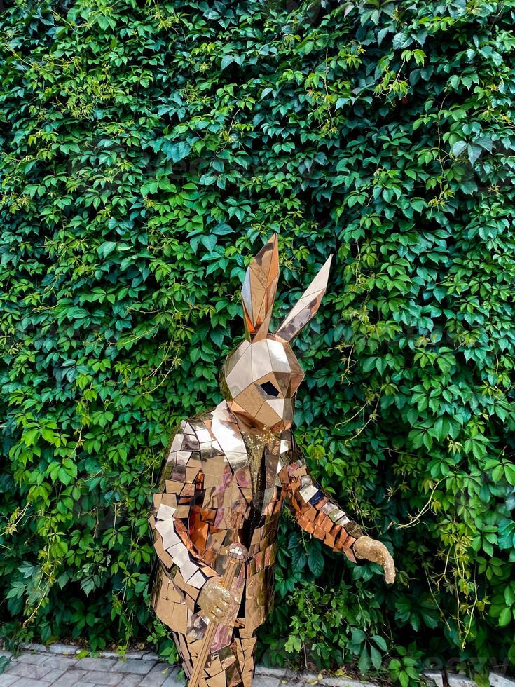 A lifesized cardboard rabbit statue stands in front of a green hedge photo