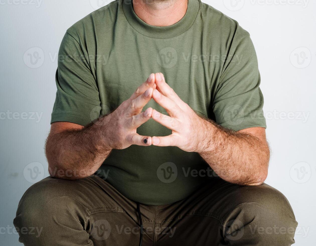 A man is wearing a bright green shirt while sitting comfortably, with his hands folded in a precise triangle shape, which conveys a strong sense of relaxation and ease in his entire posture photo