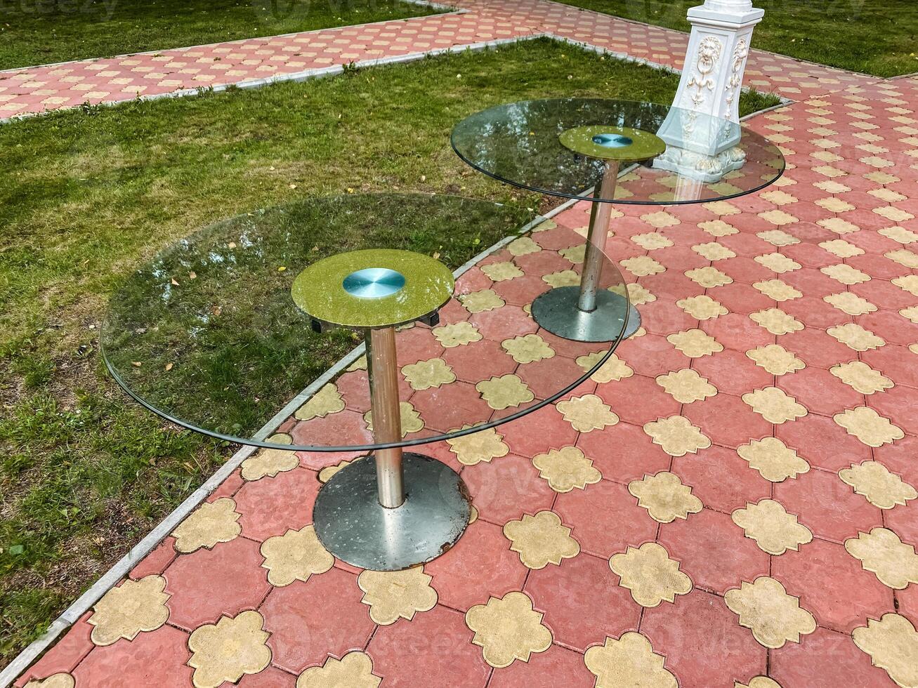 Two elegantly designed glass tables are meticulously arranged on a strong and durable brick sidewalk, forming a visually striking and appealing setup amidst the surrounding environment photo