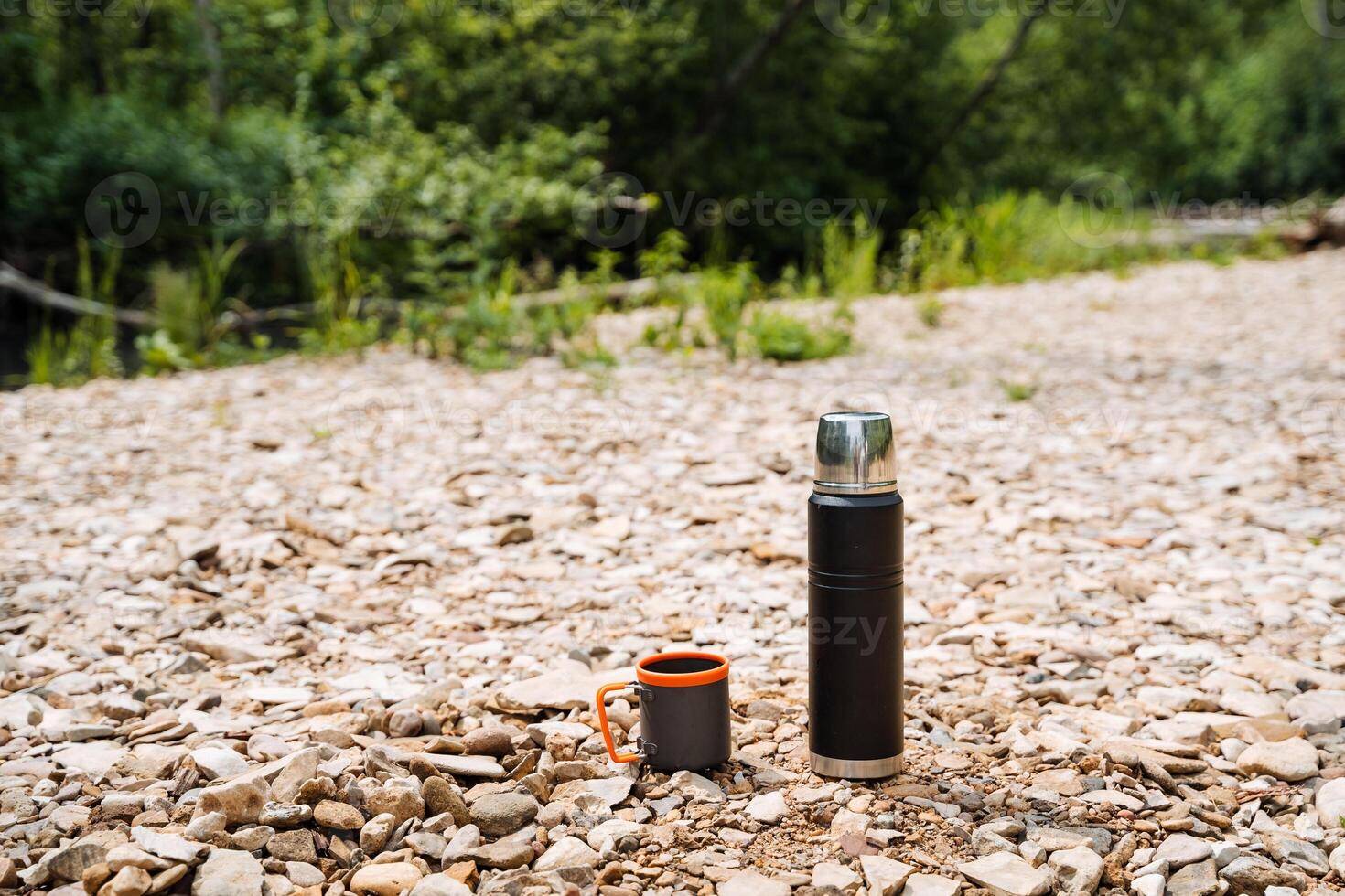 In a peaceful natural setting, there is a tranquil scene with a thermos and coffee cup placed on the ground among trees and grass, creating a sense of peace and serenity in the environment photo