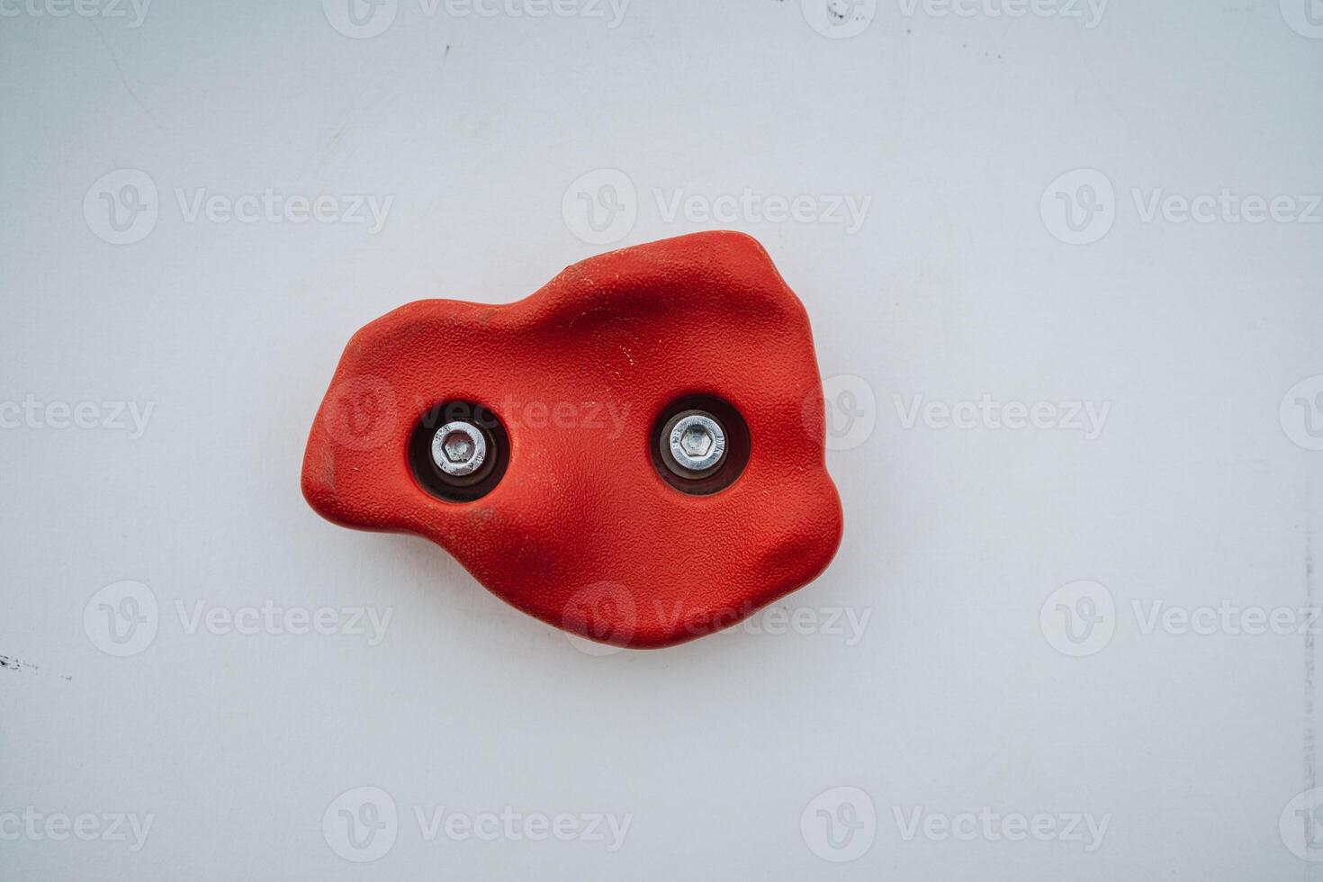 A vivid red rock adorned with two screws is prominently positioned on a clean white surface, creating a striking visual contrast that catches the eye and invites curiosity photo