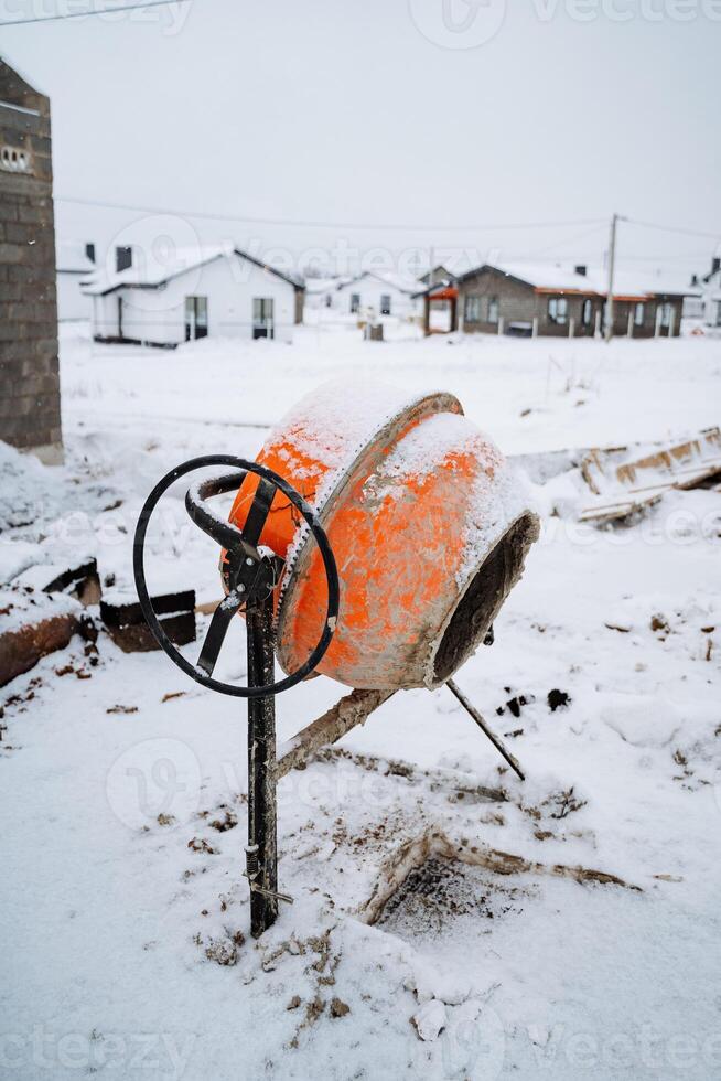 In the midst of a wintry landscape, an orange cement mixer is quietly sitting in the soft, white snow, surrounded by the chill of freezing temperatures, ice, and frosty air photo