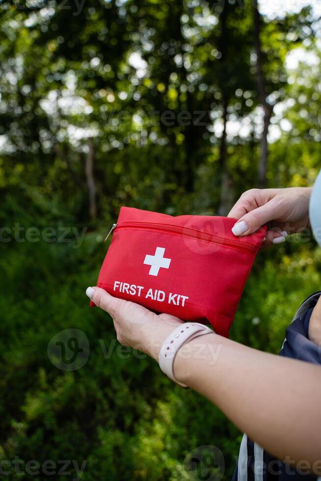 A person can be seen holding a bright red first aid kit firmly in their hand, ready to assist someone in need of medical supplies or treatment during an outdoor adventure photo