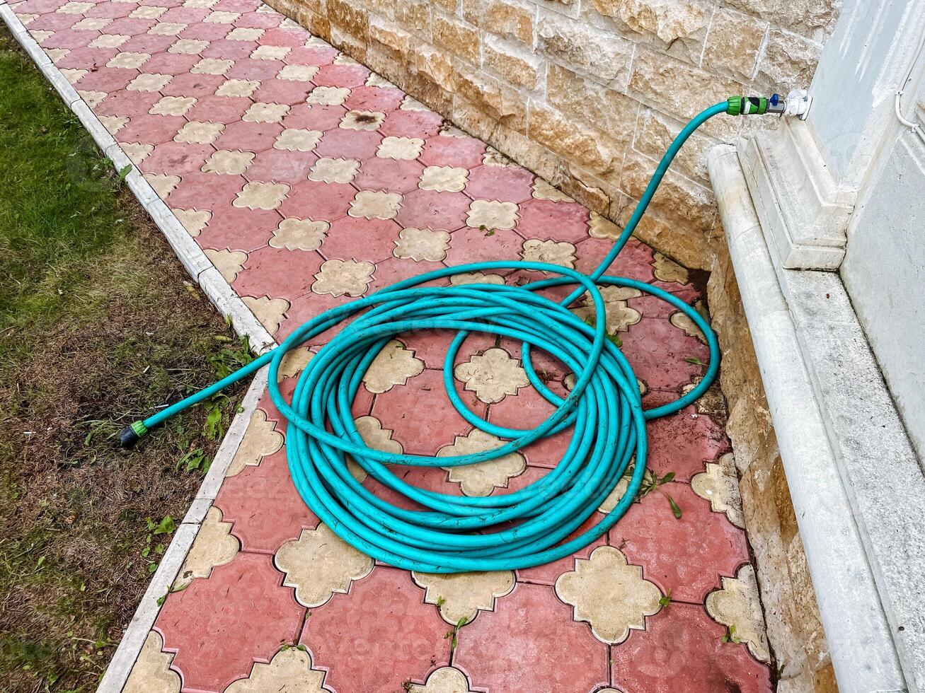 A long and vibrant green garden hose is neatly coiled and resting calmly on the sidewalk that runs parallel to a large building, catching the attention of those who pass by and admire it photo