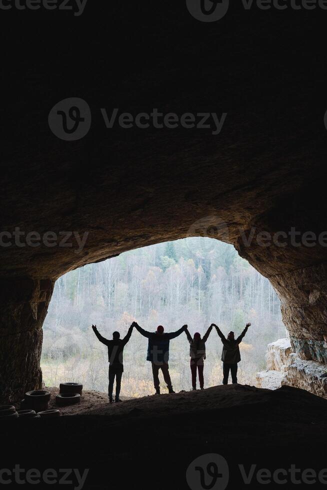 A group of people is standing together in a cave, holding hands in solidarity and friendship, creating a memorable moment in this unique and dark landscape of natures architecture photo