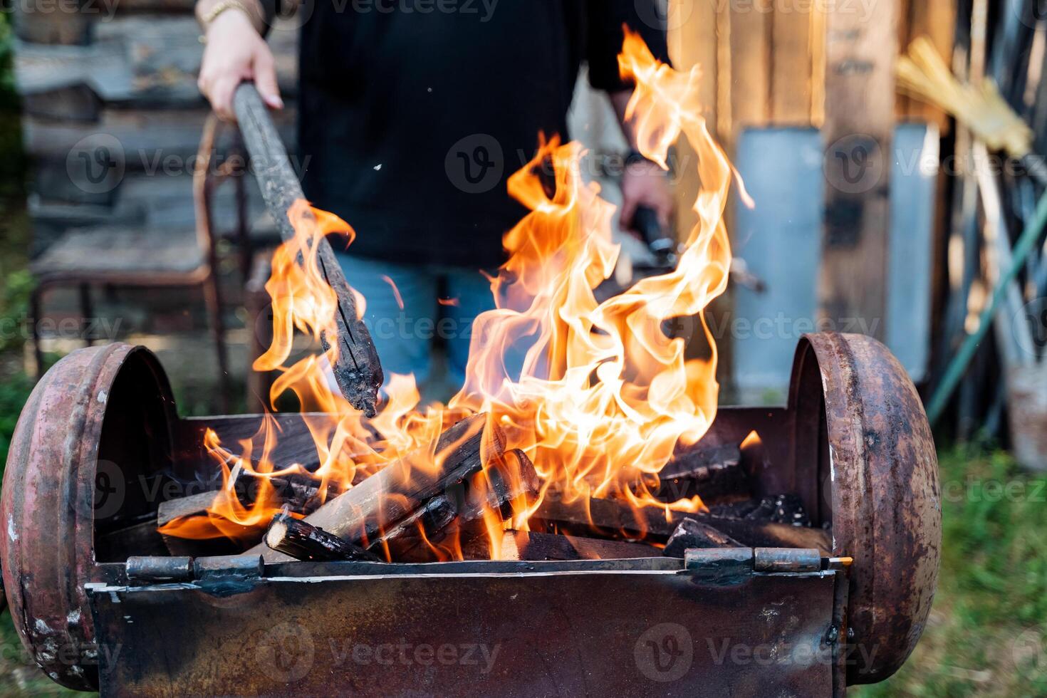 A man is cooking or working near a fire with a shovel amid flames and heat. The fire looks like it could be used for cooking or a similar activity, creating a warm atmosphere around him photo