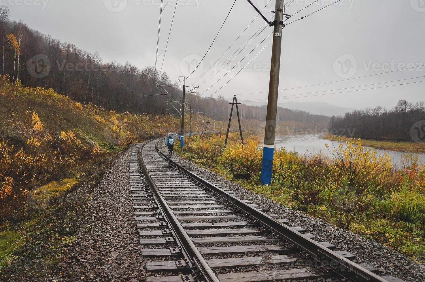A train track by the rolling river under a cloudy sky photo